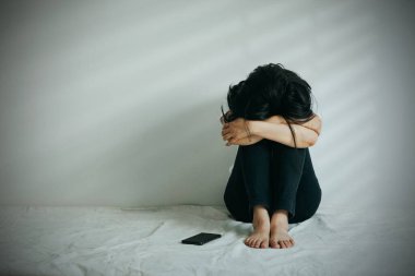 Depresyondaki kadın dizine sarılıp ağlar. Üzgün kadın, yanında bir telefonla tek başına oturdu..