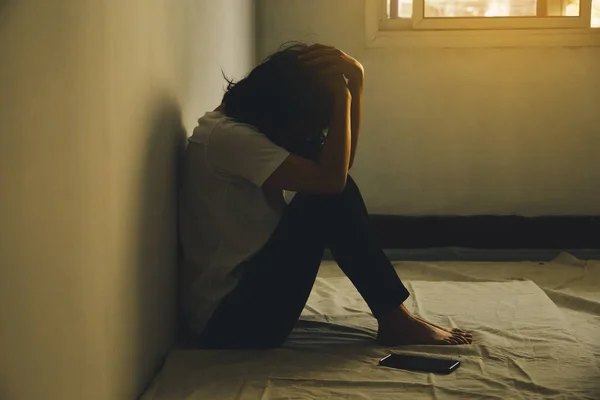 Depresyondaki kadın dizine sarılıp ağlar. Üzgün kadın, yanında bir telefonla tek başına oturdu..