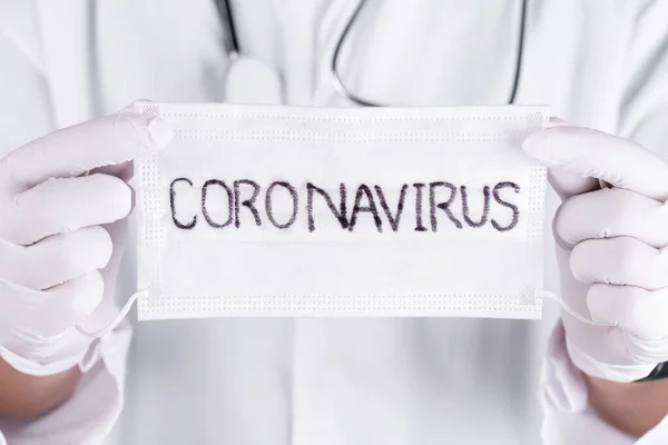Close up doctor hands holding Surgical mask with coronavirus text written on it. 2019-nCoV virus infection in Wuhan city. Covid-19 ( SARS-CoV-2 ) spread around the world. Impact of pandemic virus.