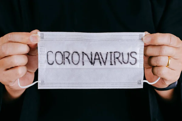 Close up hands holding Surgical mask with coronavirus text written on it. 2019-nCoV virus infection in Wuhan city. Covid-19 ( SARS-CoV-2 ) spread around the world. Impact of pandemic virus.