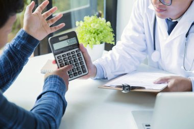 Hastaya masrafları açıklamak için hesap makinesi tutan doktor..