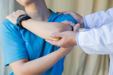 Omuz ağrısı olan kaslı bir adam fizyoterapistle egzersiz yapıyor.