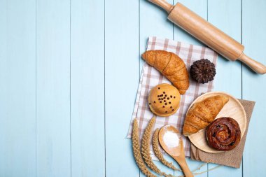 Pastane arkaplan çerçevesi. Ev yapımı ekmek ya da çörek, kruvasan ve rulo iğne, çırpı, mavi ahşap zemin üzerinde un, üst görünüm ve boşluk kopyala.