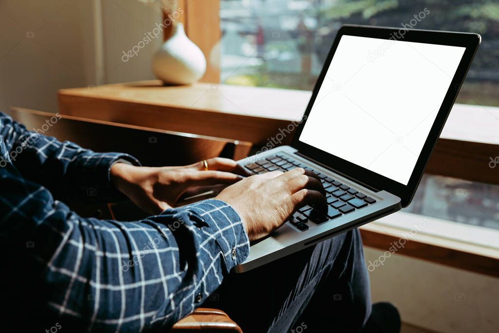 Man's hands using laptop with blank screen on desk in coffee shop.