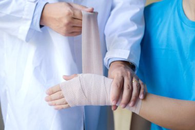 Ortopedist, erkek hastanın el eklem yerinden çıkması üzerine bilek elastik bandajı uyguluyor.