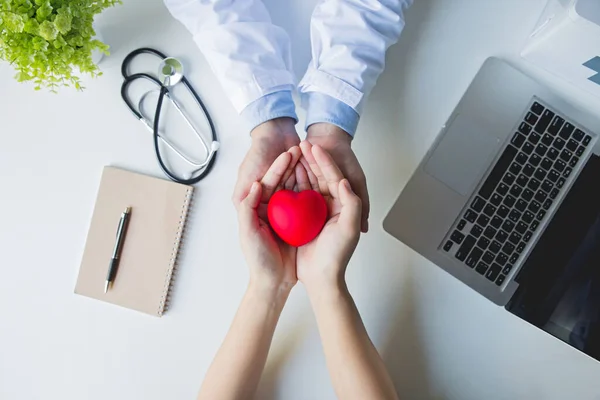 Üst görünüm: doktor ve hasta elleri beyaz masada kırmızı kalbi tutuyor, sağlık hizmeti, sevgi, umut ve aile kavramı, dünya kalp günü, dünya sağlık günü