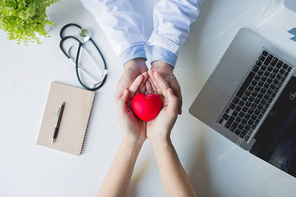 Top view .doctor and patient hands holding red heart on white table, health care love, give, hope and family concept, world heart day,world health day