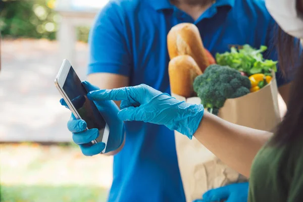 Woman appending signature in digital mobile phone after Grocery store delivery man wearing blue shirt delivering food to a woman at home.delivery service during covid19.New normal.