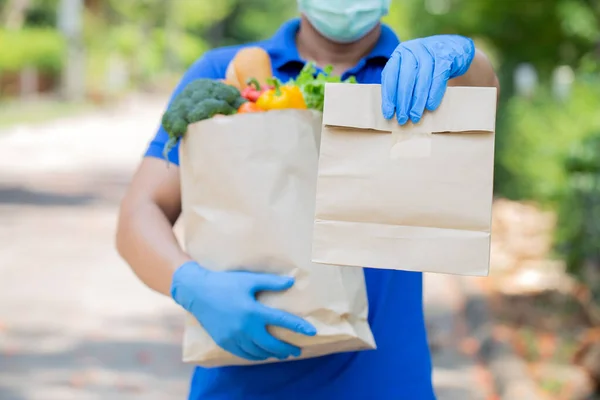 Delivery man holding paper bag with food  in front of the house , food delivery man in protective mask and protective gloves.disease outbreak, coronavirus covid-19 pandemic conditions.