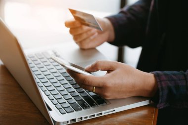 Çevrimiçi ödeme yapmak için ellerini kapat. Adamın elleri kredi kartı tutuyor ve online alışveriş için akıllı telefon kullanıyor.