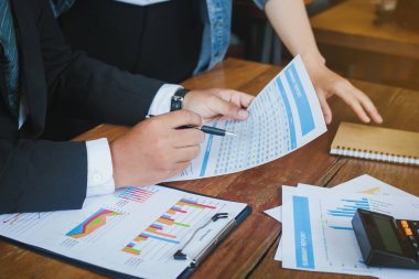 İş adamları yorum yapıyor, büyüme grafikleri gösteriyor ve ofiste iş konuşmaları yapıyorlar. Şirket büyümesi tartışılıyor