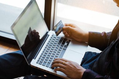 Genç adam dizüstü bilgisayar kullanıyor ve kredi kartı ödemelerini internet üzerinden yapıyor. Ev konseptinde çalışıyor..