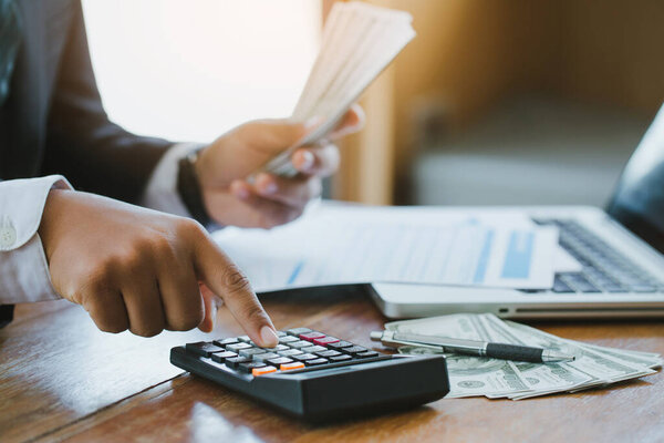 Бизнесмен, использующий калькулятор и держащий деньги, рассчитывает коммерческие расходы.