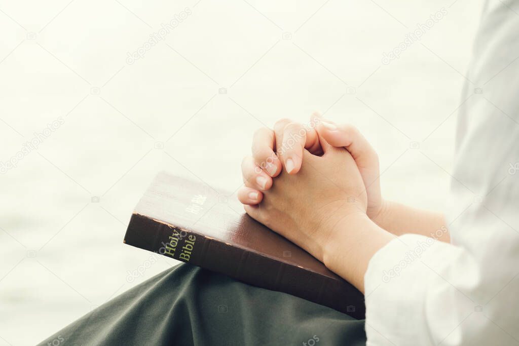 Woman's hands clasped in prayer over a closed Bible prayer and thank God.Christian Religion concept background.