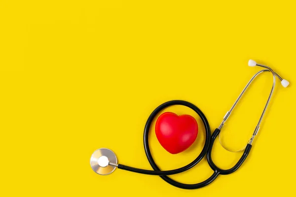 Sarı arka planda steteskoplu kırmızı kalp, sağlık sigortası konsepti, dünya sağlık günü, dünya kalp günü konsepti.