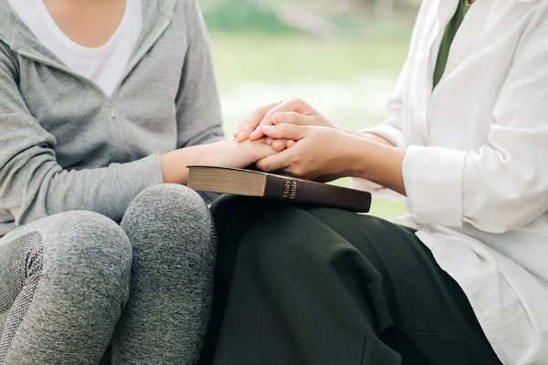 Two women holding hands over holy bible praying worship believe.