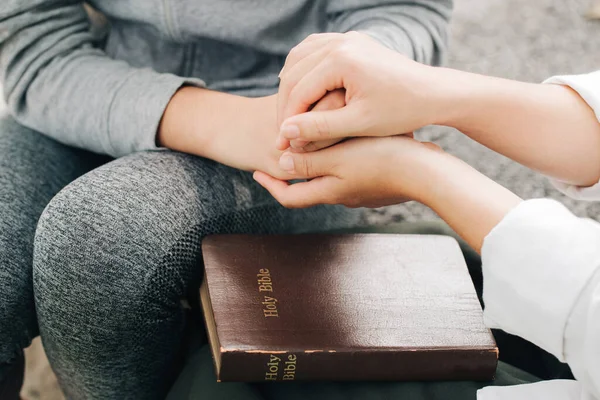 Two women holding hands praying worship believe.Holly bible