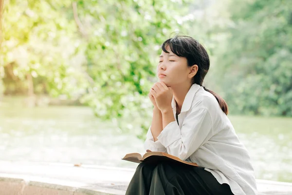 Woman praying in the morning on nature background.Hands folded in prayer on a Holy Bible in church concept for faith, spirituality and religion