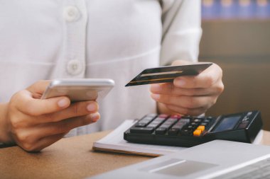 Kredi kartı tutan ve akıllı telefon kullanan bir kadın. Çevrimiçi alışveriş, e-ticaret, internet bankacılığı, harcama, ev konseptinden çalışma