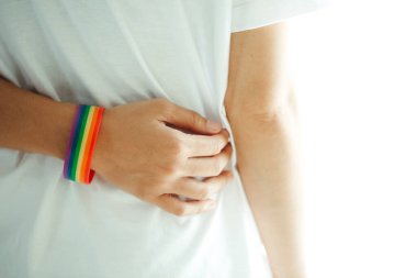 Gökkuşağı desenli bileklik takan, kucaklayan ve sarılan ellerin yakın çekimi. LGBT kavramı.