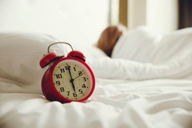 Yataktaki çalar saat ve arka planda uyuyan kadın.