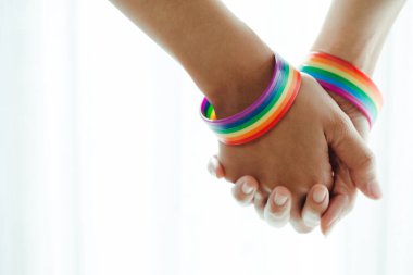 Bileklerinde gökkuşağı desenli bir bilekle el ele tutuşan lezbiyen çift. LGBT, aktivizm, toplum ve özgürlük kavramı..