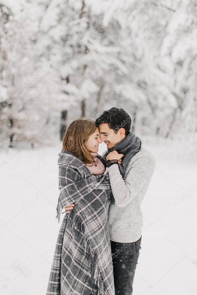 Couple in love walking in the snowy forest, hugging, kissing and enjoying.
