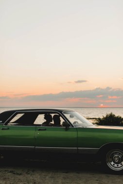 Gün batımında okyanusun kenarında bir arabada aşık bir çiftin silueti.