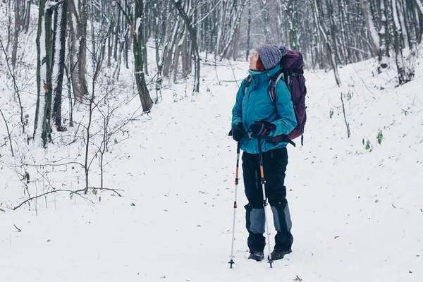 Ung flicka med stor ryggsäck ser vintern undan skogsvandringar — Stockfoto