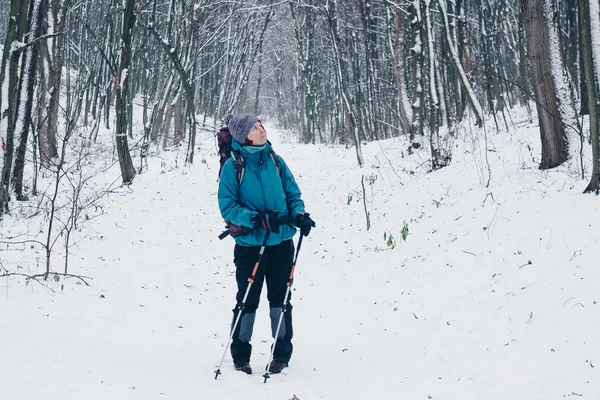 Ung flicka med ryggsäck och trekking stolpar ser vintern undan skogsvandringar — Stockfoto