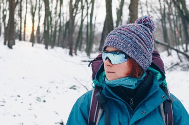 Sırt çantası ve güneş gözlüğü ile genç kız kış orman yoluyla bir yana hiking görünüyor