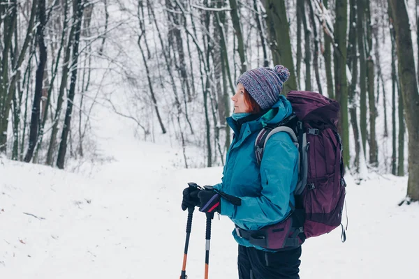 Ung flicka med ryggsäck ser parentes stående i skogen vinter — Stockfoto