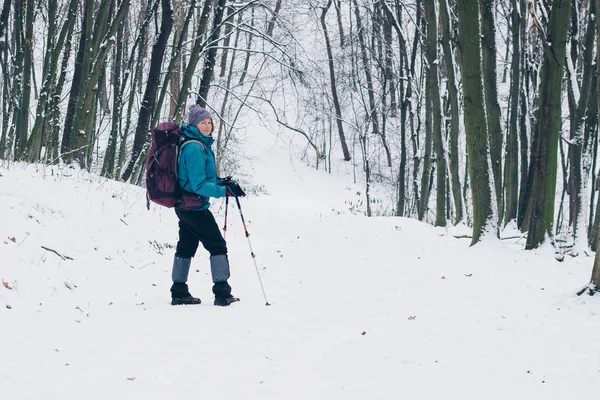 Ung flicka med ryggsäck som vänder på stigen i skogen vinter — Stockfoto