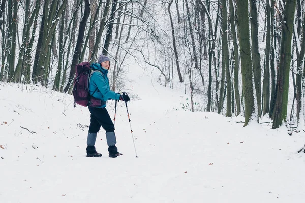 Ung flicka med ryggsäck som vänder medan vandring på stigen i skogen vinter — Stockfoto