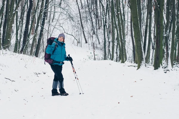 Ung flicka med ryggsäck vänder bor på stigen i skogen vinter — Stockfoto