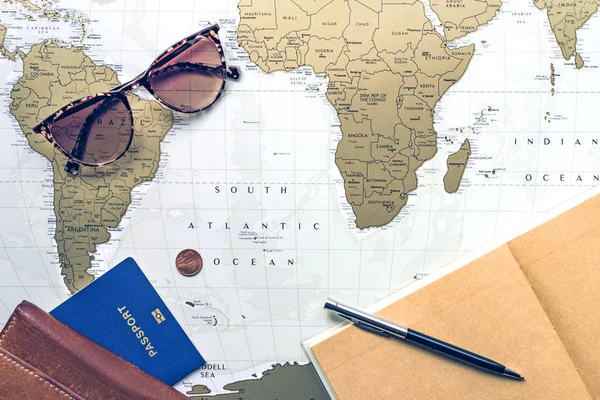 Travel flatlay: wallet, pocketbook, passport, pen and sunglasses on world map