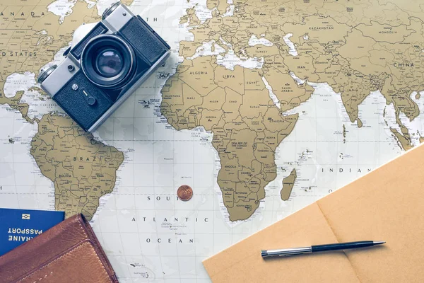 Travel flatlay with wallet, pocketbook, passport, pen, coin and camera on the world map on the background