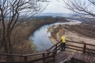 Bulutlu bir günde sarı ceketli büyük nehre bakıp bakan bir adam.
