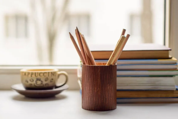 Cup of coffee, books, pencils in the pencil box on the windowsil