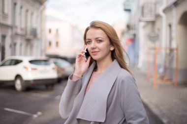 Şehir caddesinde cep telefonuyla konuşan kızıl saçlı şık bir kız.