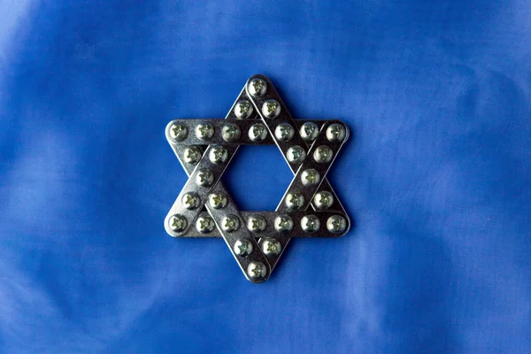 Judaism: shiny star of David, built with meccano, lies on blue fabric, top view, single light source, partial dimming