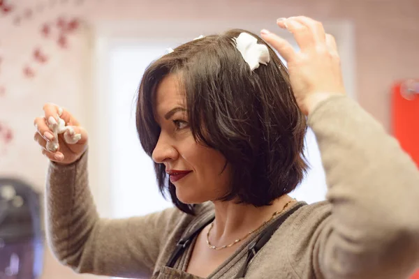 woman with black hair does her hair at the dressing table with a mirror
