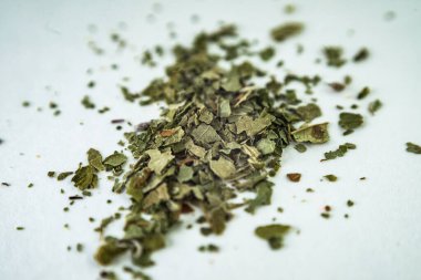 Beyaz bir yüzey üzerinde yeşil kuru yapraklar (marihuana, tütün)