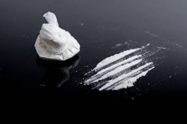 Beyaz toz (eroin, kokain, narkotik) siyah bir zemin üzerinde plastik bir torba içinde, uyuşturucu bir iz şeklinde dağılmış