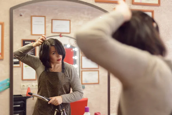 woman with black hair does her hair at the dressing table with a mirror