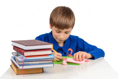 Çocuk gelişimi: mavi tişörtlü bir okul çocuğu masaya oturur ve renkli kağıtlara resim çizer, bir yığın ders kitabı ve kağıt, origami