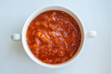 Beyaz arka planda iki sapı olan beyaz bir kasede kırmızı tabak.