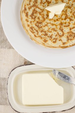 Karnaval kutlaması: taze pişmiş gerçek Rus gözlemeleri yoğurtla, beyaz bir tabakta, tereyağında ve bıçakta yapılır. Keten masa örtüsü, kapat, üst görünüm, dikey konum