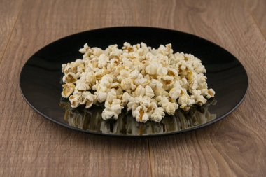 Mikrodalgada ev yapımı. Siyah bir kasede patlamış mısır. Tahta bir masada.