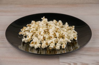 Mikrodalgada ev yapımı, siyah bir kasede patlamış mısır beyaz ahşap bir masada, ön tarafta.